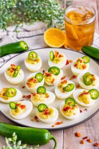 deviled eggs with bacon and jalapenos on a plate next to pickles