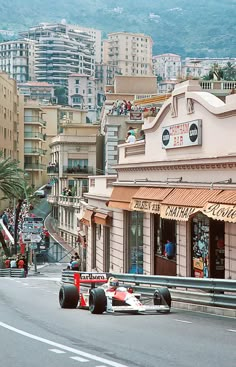 a man driving a race car down a street next to tall buildings and palm trees