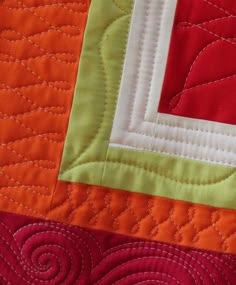 an orange, red and green quilt with white stitching