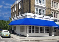 an old car is parked in front of a building with blue awnings on the roof