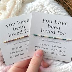 two small cards with the words you have been loved for written on them in gold and green beads