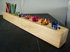 a row of colored crayons sitting on top of a wooden shelf next to a white wall