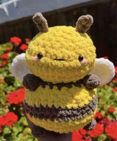 a crocheted stuffed bee is held up in front of some red and yellow flowers