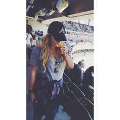 a woman standing in front of a baseball stadium holding a drink and looking at the camera