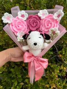 a hand holding a small stuffed animal with flowers on it's head and pink ribbon around its neck