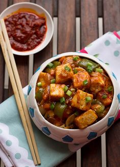 a bowl filled with tofu and vegetables next to chopsticks on a table