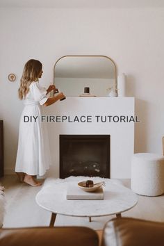 a woman standing in front of a fireplace next to a white table and brown chairs