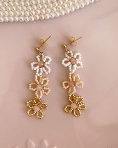 Our Beaded Pastel Flower Drop Earrings are a delightful and charming addition to your jewelry collection. They feature a cascade of delicate pastel-hued beads intricately arranged in the form of flowers, creating a playful and feminine design. The beaded flowers gently dangle, adding subtle movement and a touch of whimsy to your look. Whether you are dressing up for a special event or adding a touch of color to your everyday style, they are a versatile and eye-catching accessory. Details & Care Handmade Feminine Flower Shaped Earrings, Handmade Feminine Flower Earrings, Handmade Feminine Flower-shaped Earrings, Handmade Cream Flower Earrings, White Beaded Flower-shaped Earrings For Gifts, Dainty White Beaded Earrings For Gifts, Dainty Handmade Flower Earrings, Flower Drop Earrings, Drop Earrings Gold