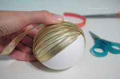 a hand holding a ball with gold foil on it next to some scissors and tape