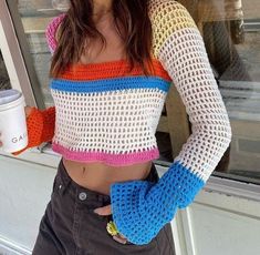 a woman standing in front of a window holding a coffee cup and wearing a crocheted crop top