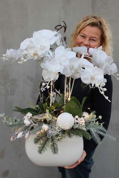 a woman holding a white vase filled with flowers