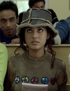 a woman wearing a hat sitting next to other people in front of a classroom desk