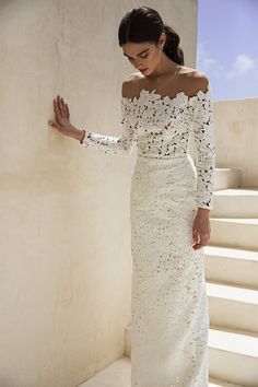 a woman in a white dress leaning against a wall with her hand on her hip