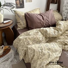 a bed covered in blankets and pillows next to a table with a potted plant