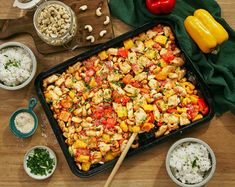 a pan filled with chicken and vegetables next to bowls of rice, peppers, garlic, and seasonings