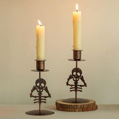 two candles are sitting next to each other on a table with a candle holder in the shape of a skeleton