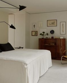 a white bed sitting in a bedroom next to a wooden dresser and lamp on top of it