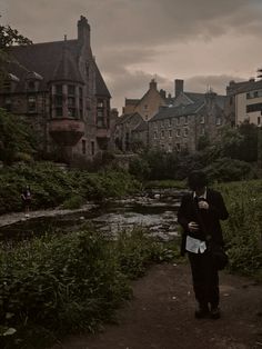 a man in a tuxedo is standing on a path near a river and buildings