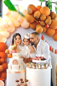 a man and woman holding a baby in front of a cake with oranges on it