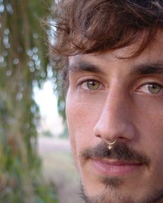 a close up of a person with a nose ring on his nose and trees in the background