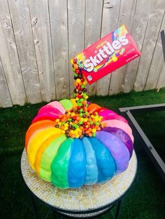 a rainbow colored cake sitting on top of a table next to a sign that says skittles