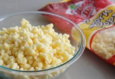 a bowl filled with corn kernels next to a bag of cheesy popcorn