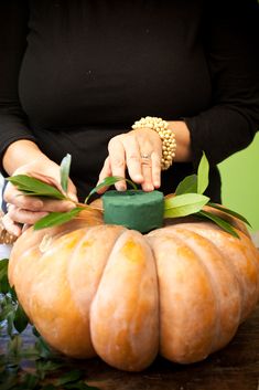 a woman is decorating a pumpkin with green leaves on the table in front of her