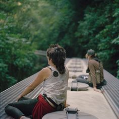 two people are sitting on the edge of a bridge looking down at trees and water