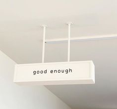 a sign that says good enough hanging from the ceiling in a room with white walls