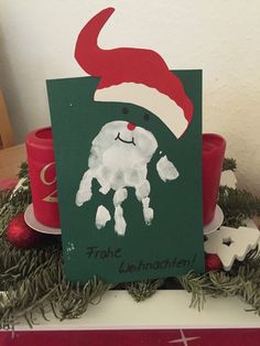 a christmas card with a santa hat on it and a hand print in the middle