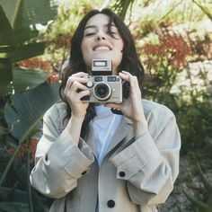 a woman taking a selfie with her camera in front of some trees and plants