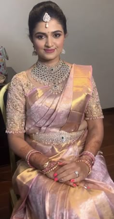 a woman in a pink and gold sari sitting on a chair with her hands crossed