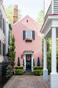 a pink house with black shutters and white trim on the front door is surrounded by greenery