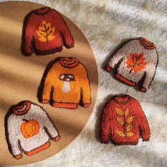 three knitted sweaters with autumn leaves on them sitting next to a round plate