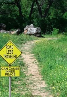 a road less traveled sign on the side of a dirt path near trees and grass