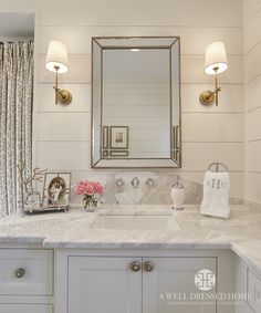 a white bathroom with marble counter tops and gold accents on the mirror above the sink