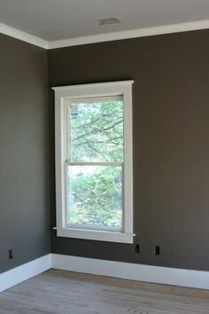 an empty room with a window and hard wood floor in the foreground is painted gray