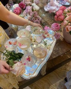 a woman is holding a tray full of flowers and glasses with water on it in front of other vases