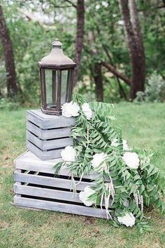 a wooden crate with flowers and a lantern on top is sitting in the grass near some trees