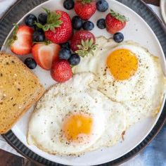 two fried eggs and toast on a plate with strawberries, blueberries and strawberries