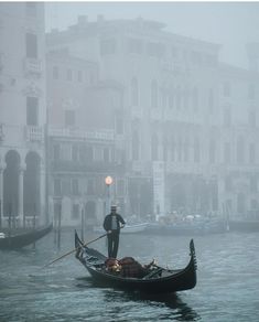 a man riding on the back of a gondola down a river next to tall buildings