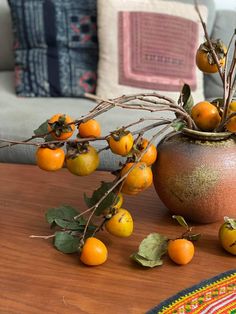 oranges are on the table next to a vase with branches and fruit in it