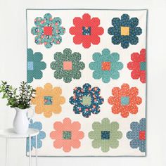 a colorful quilt hanging on the wall next to a vase with a plant in it