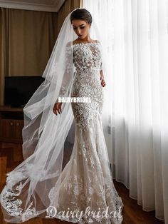 a woman in a wedding dress standing by a window with a veil on her head