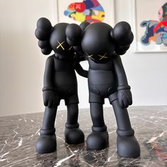 two black figurines standing next to each other on a marble counter top in front of paintings