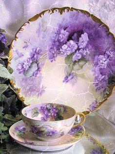 purple flowers are in the center of this tea cup and saucer