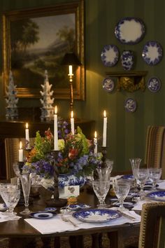 a dining room table is set with blue and white plates, candles, and flowers