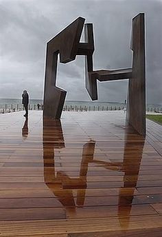 a person standing in front of a sculpture on top of a wooden floor next to the ocean