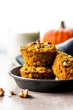 some muffins are stacked on top of each other in a black bowl next to a glass of milk