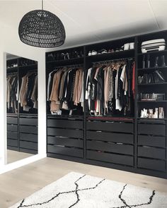 an organized closet with black drawers and clothes hanging on the wall, along with a white rug